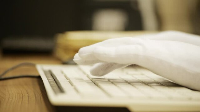 a user wearing white gloves is typing something on a white computer keyboard
