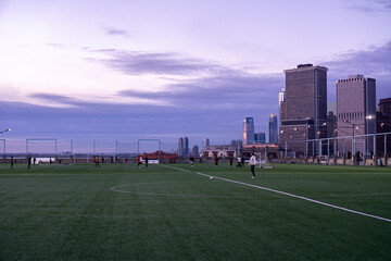 New York City, USA - December 18, 2021: Pier 5 soccer field in Brooklyn. Turf field with people playing soccer at sunset with view of tall modern buildings © Renata