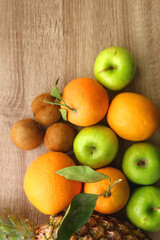 Pineapple, apples, oranges, lemons and kiwis on a wooden table. Top view.