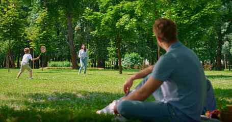 Young father watching badminton game blurred view. Activity on fresh air in park
