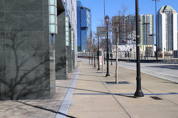 Fototapeta na wymiar a smooth sidewalk lined with bare winter trees and tall black light posts and an empty street with office buildings and skyscrapers in the city skyline in downtown Atlanta Georgia USA