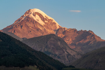 A panoramic morning view on Mount Kazbegi in the Greater Caucasus Mountains in Georgia. Clear sky over the snow-capped summit. Khokh range. Sunset, sunrise. Mystical. Adventure and discovery