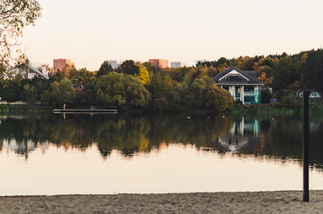 Fototapeta premium Autumn landscape near the lake. There are houses on the shore of the lake. You can see city houses in the distance.