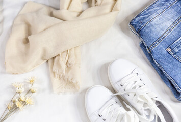 Blue jeans scarf, bag and white sneakers on white bed. Women's stylish summer or spring outfit. Trendy fashion clothes. Flat lay, top view.