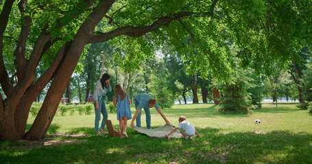 Young family picnic on lawn grass. Parents preparing lunch with two children.