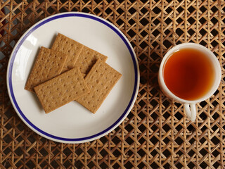 Obraz na płótnie Canvas Crispy coffee biscuits and a cup of black tea on woven cane background, flat lay view. Lit by window light.