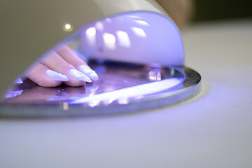 Client in manicure salon dryes gel polished nails in UV light

