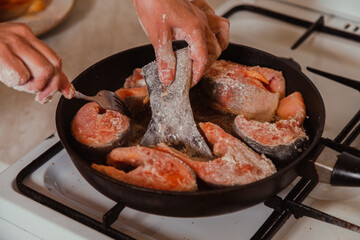 Adding fish tail to pan full of raw salmon cooking on hot pan with sizzling oil