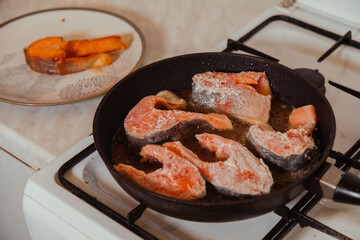 Many pieces of raw salmon fish frying on hot pan with sizzling oil at home kitchen