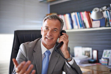He just received some great news. Shot of a mature businessman looking pleased while talking on the phone in his office.