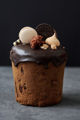 Glazed chocolate easter cake decorated with macaroons and candies on dark background, copy space. Happy Easter holidays. Kulich