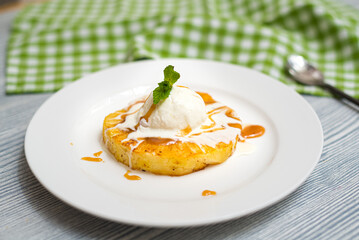 A ball of creamy vanilla ice cream on a slice of fried pineapple with caramel sauce. One serving on...