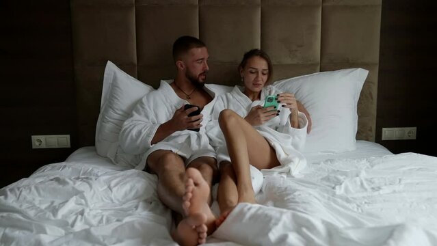 a couple in white coats is lying in bed with phones. front view. the general plan