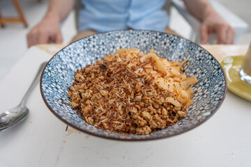 Bowl with granules and coconut and chocolate chips for a healthy breakfast. Male hand with a spoon and a plate with muesli