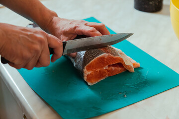 Hand cutting raw headless salmon fish laying on blue cutting board at home