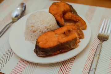 A plate of homemade cooked salmon with rice on white plate on the table