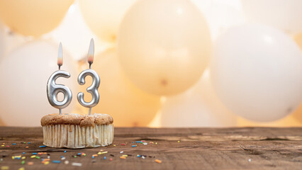 Happy birthday card with candle number 63 in a cupcake against the background of balloons. Copy space happy birthday for sixty three years old.