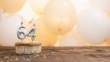 Happy birthday card with candle number 64 in a cupcake against the background of balloons. Copy...