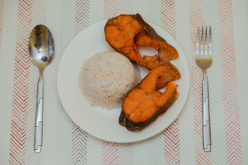 A plate of homemade cooked salmon with rice on white plate on the table