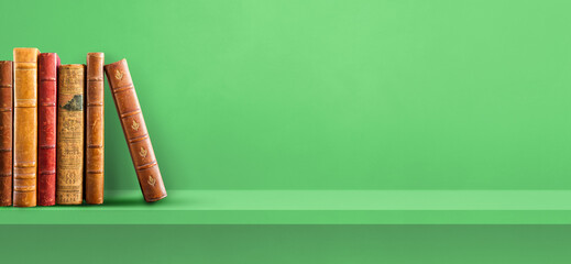 Row of old books on green shelf. Background banner