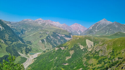 Distant view on the Gudauri Arch in Georgia- the Russia Georgia Friendship Monument or Treaty of Georgievsk Monument. Green mountains of the Greater Caucasus Mountain Ranges. Georgian Military Road