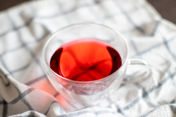 Clear cup of red raspberry tea on a white plaid tablecloth