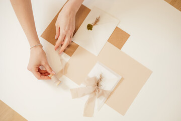 Obraz na płótnie Canvas Cropped photo woman hand, peach composition paper envelopes, ribbons, tape reel, wax, cut out handmade jobbing.