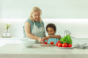 Mature woman and little child with black hair in white kitchen. Healthy eating concept.
