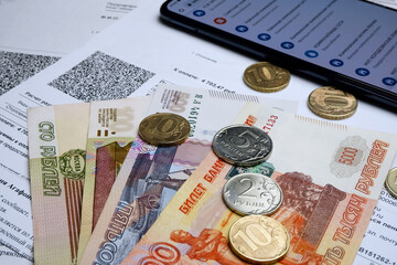Utility payments via a mobile application in a smartphone.Russian money and a smartphone on the background of receipts for heating.