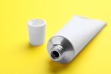 Open white tube of ointment on yellow background, closeup