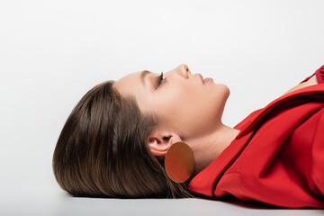 side view of trendy young woman in red blazer lying on grey.