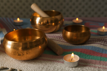 Tibetan singing bowls with mallets and burning candles on colorful fabric