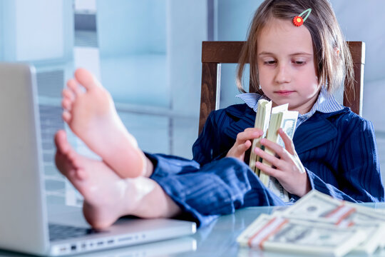 A beautiful young business girl put her feet up on a table and plays with US Dollar money.  Horizontal image.