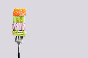 Close-up of fork with food on it: delicious fillet salmon, cucumber, onion, green salad on gray...