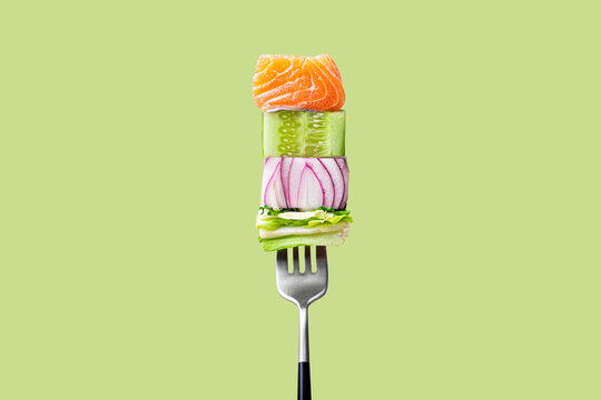 Naklejki Close-up of fork with food on it: delicious fillet salmon, cucumber, onion, green salad on green background. Concept of healthy diet and clean eating, balanced nutrition space for text