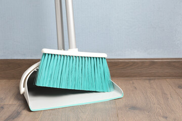 Plastic broom with dustpan near light blue wall indoors - obrazy, fototapety, plakaty