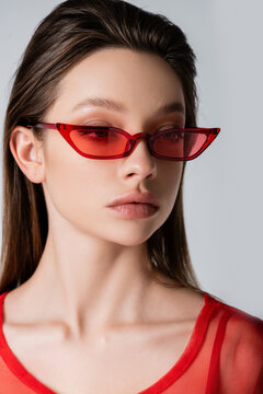 young model in red trendy sunglasses isolated on grey.