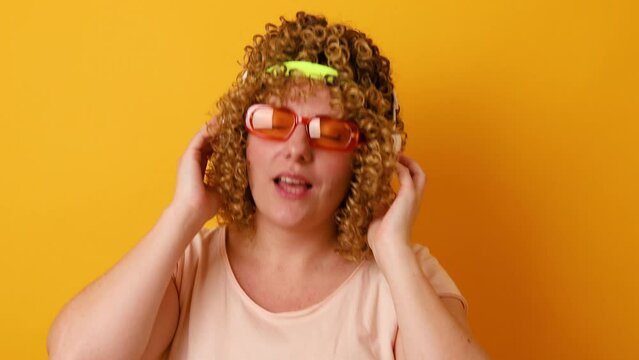 Funny cheerful wavy haired girl with glasses and a bandage listening soul dancing having fun isolated over yellow color background