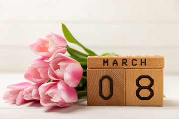 International Women's Day.Beautiful card for March 8.Spring bouquet of pink tulips with a wooden calendar on a white textured wood. Holiday concept.Copy space.