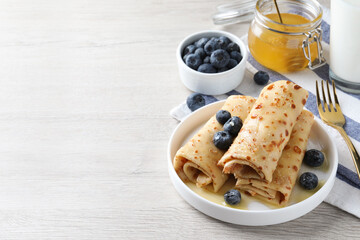 Delicious crepes served with blueberries, honey and milk on white wooden table. Space for text