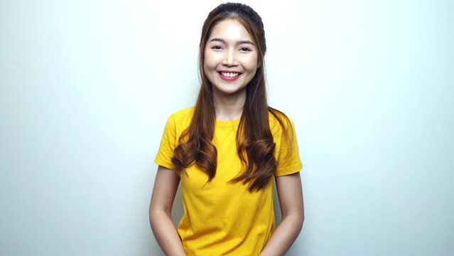 Happy young Asian woman in yellow t-shirt looking to camera and smiling joyfully, white background.