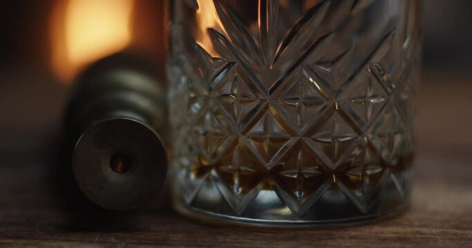 Fire reflects in a monoculars eye next to a near empty glass of bourbon.