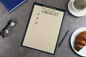 Clipboard with inscription Checklist, eyeglasses, cup of coffee and croissant on grey table, flat lay