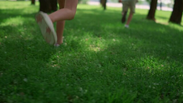 Running children legs on green grass meadow. Unknown kids play jogging outdoors.