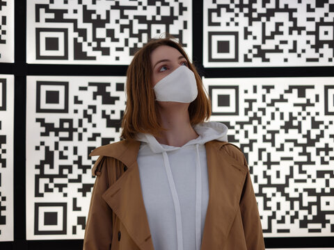 woman in a white protective mask against the background of large qr codes
