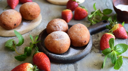 Sweet dessert: Delicious strawberry donuts sprinkled with powdered sugar for breakfast for the whole family on a wooden plate with strawberries on a gray background. Close-up