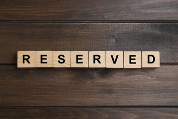 Word RESERVED made with cubes on wooden surface, top view. Table setting element