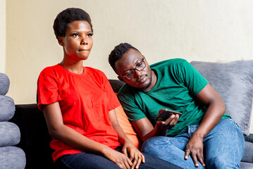 young african couple sitting together on the sofa with a mobile phone.