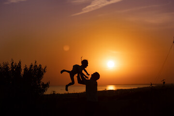 Fototapeta na wymiar Silhouette of a man and a child against the sunset.Dad raises his son 