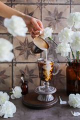 Cold coffee with cream. A woman's hand pours milk into strong iced coffee. Breakouts and splashes.